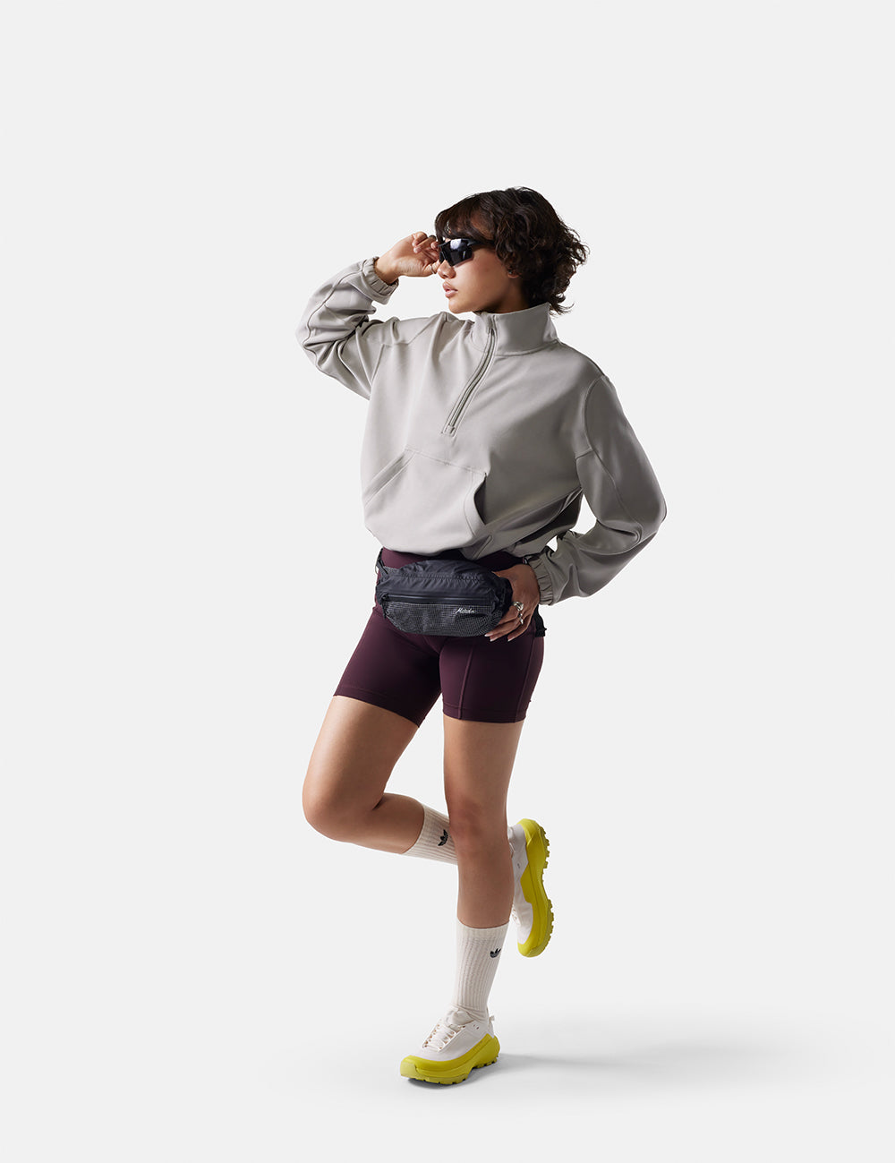 Person wearing a gray jacket, maroon shorts, and white sneakers on a white background