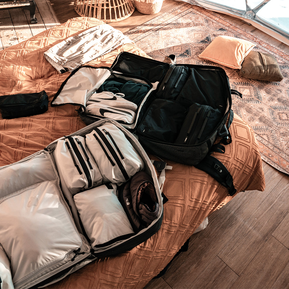 Travel packs full of gear and packing cubes laying on cozy bed