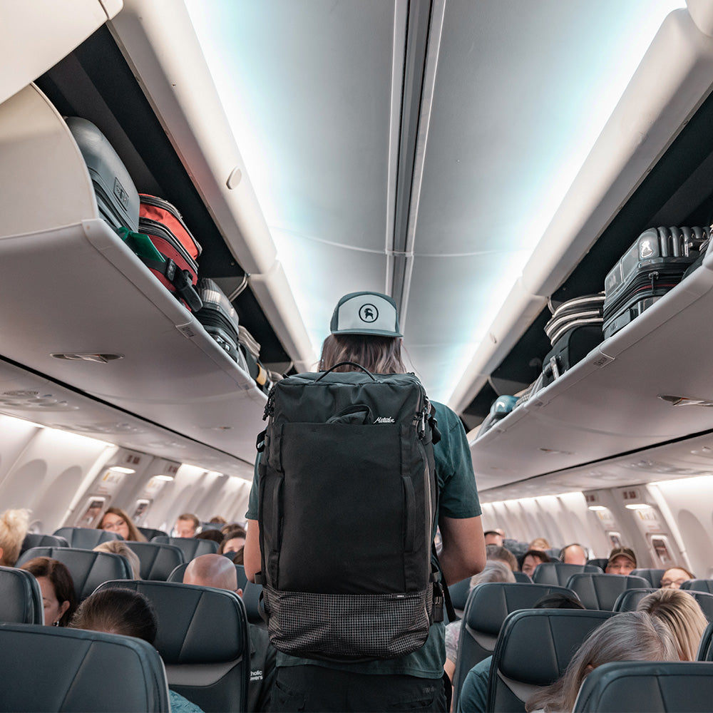man with black backpack, walking down airplane aisle 