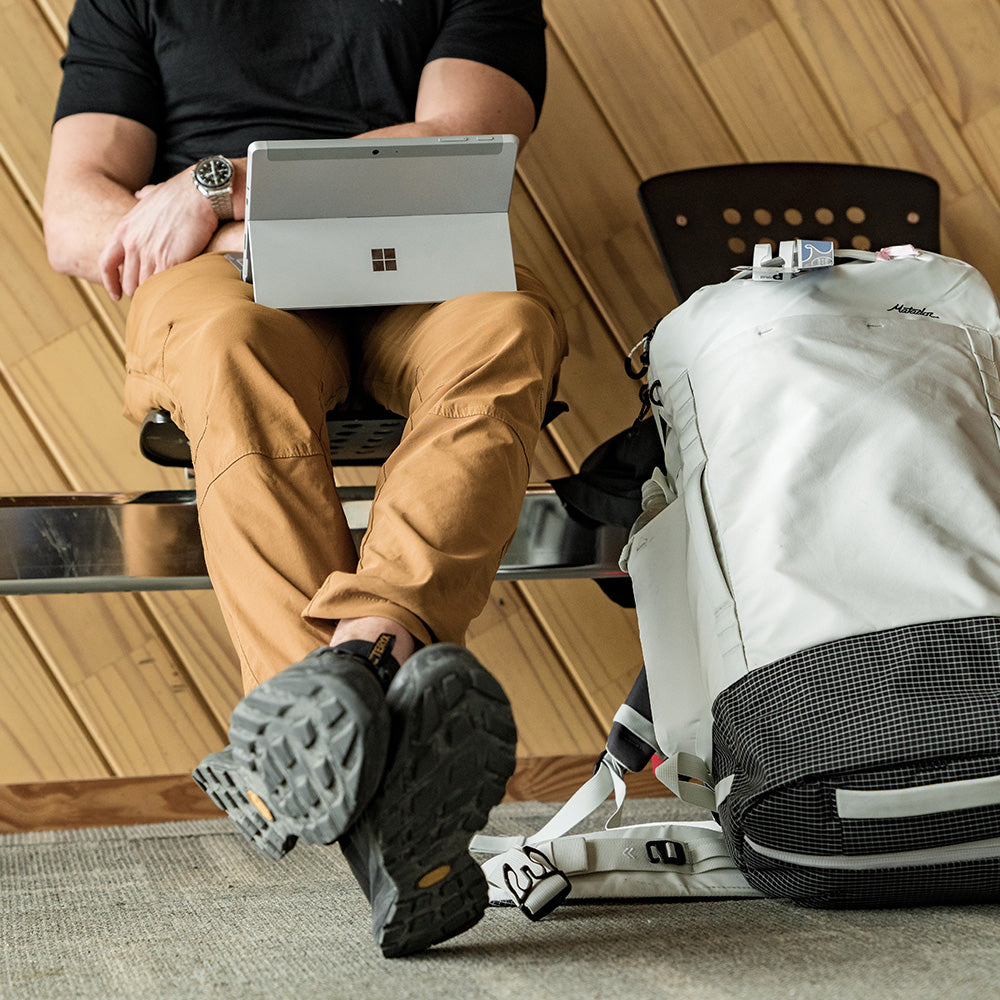 man sitting on bench with computer, a white backpack on the floor next to him