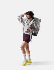 Person wearing a gray jacket, purple shorts, and white sneakers with a backpack on a white background