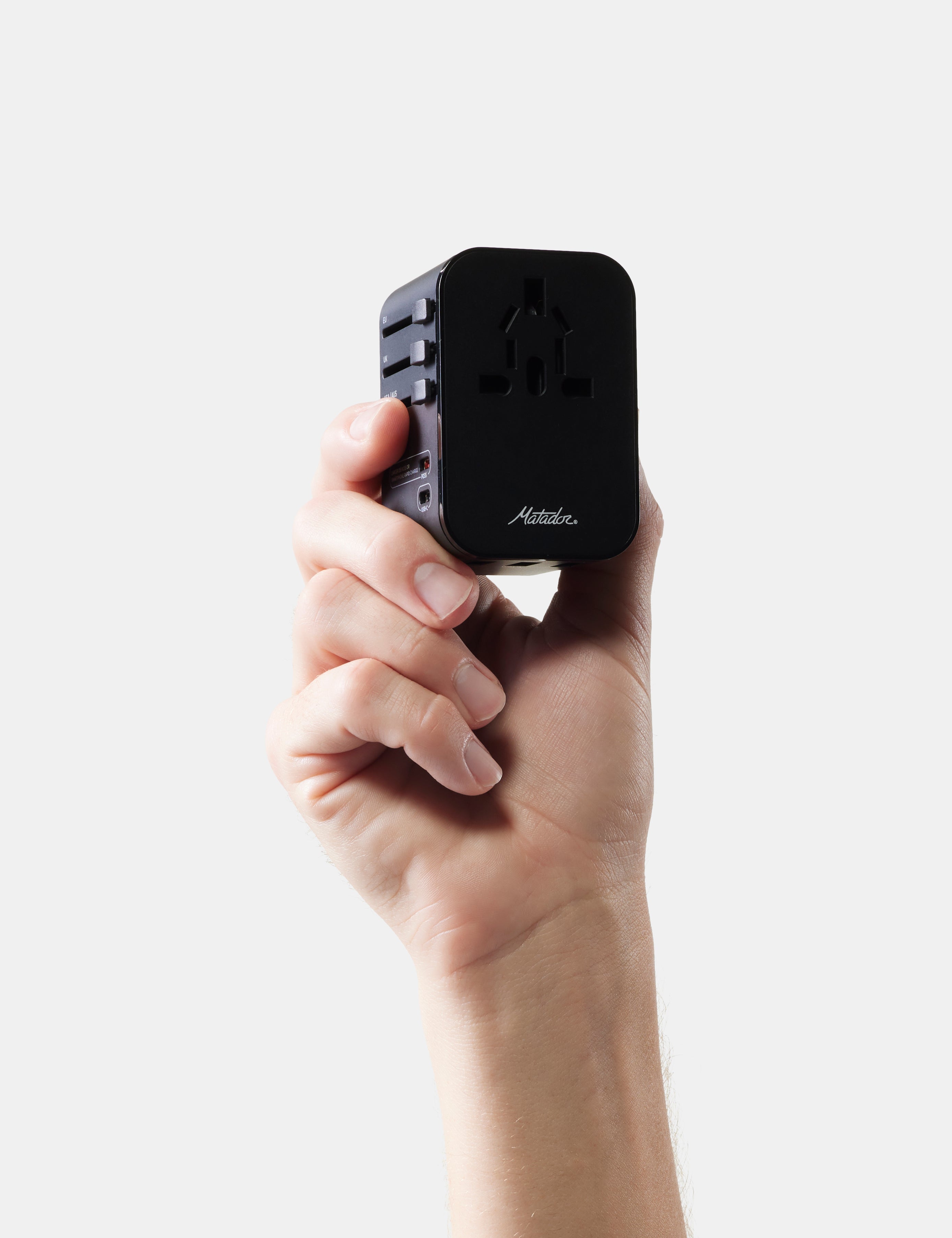 Hand holding a black travel adapter with 'Matador' branding on a white background