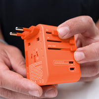 close up view of hands holding orange travel adapter, pushing EU prong slider out