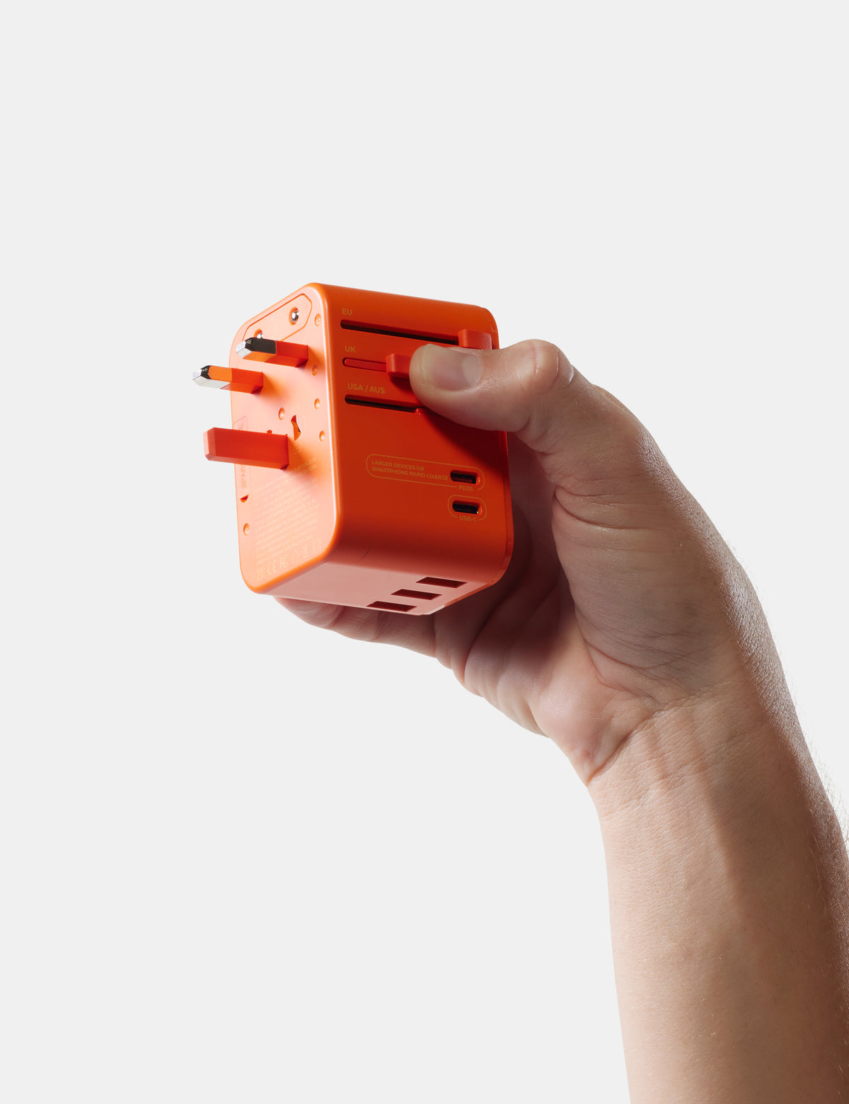 Hand holding an orange travel adapter against a white background