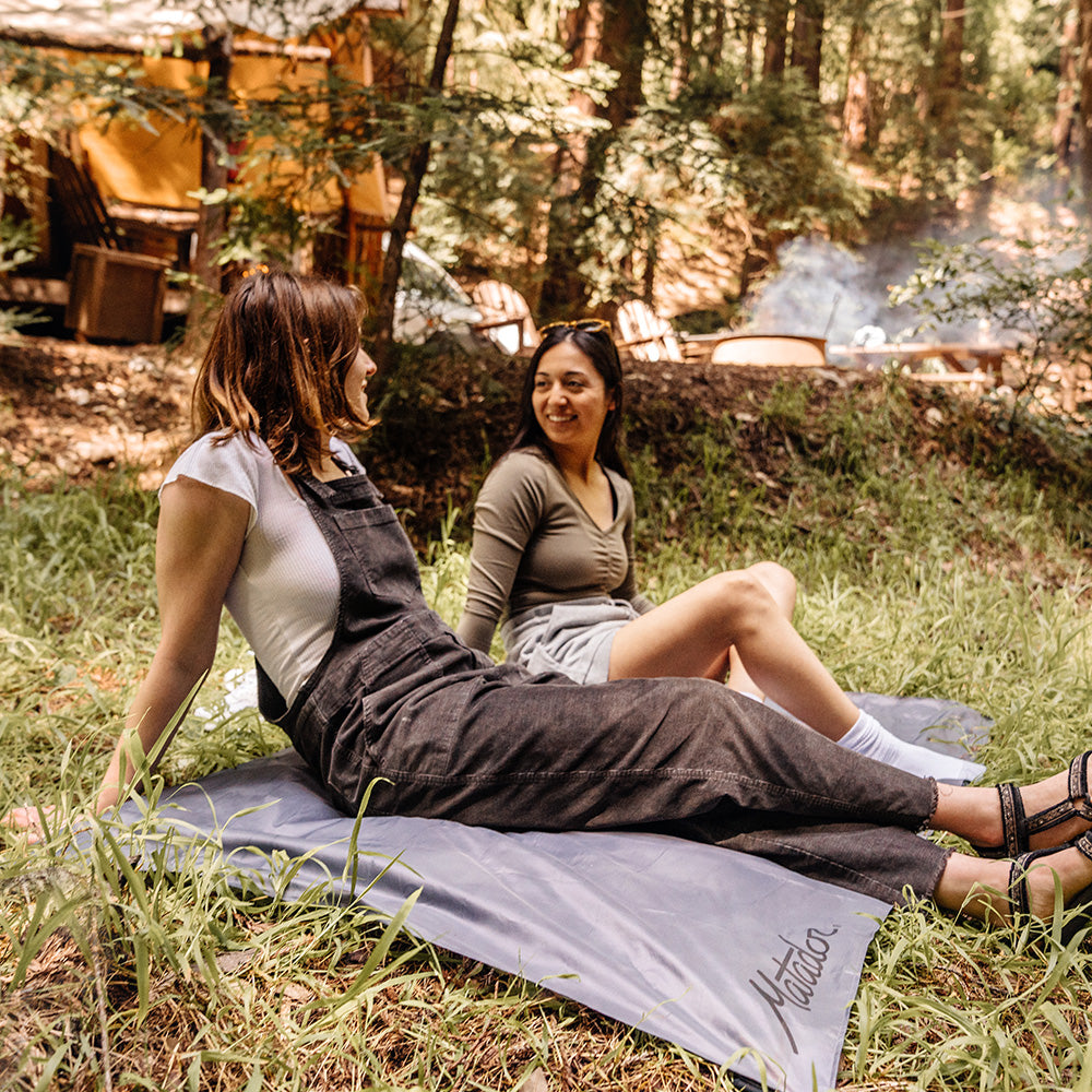 two women sitting on pocket blanket in the woods