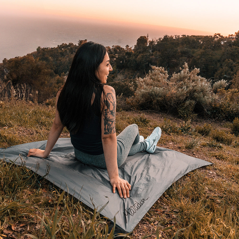 woman sitting on pocket blanket looking out at coastline