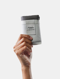 Hand holding a white pocket blanket on a light gray background