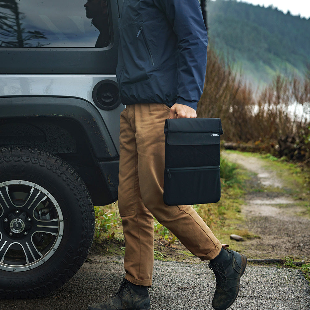 man walking to vehicle carrying laptop base layer from handle