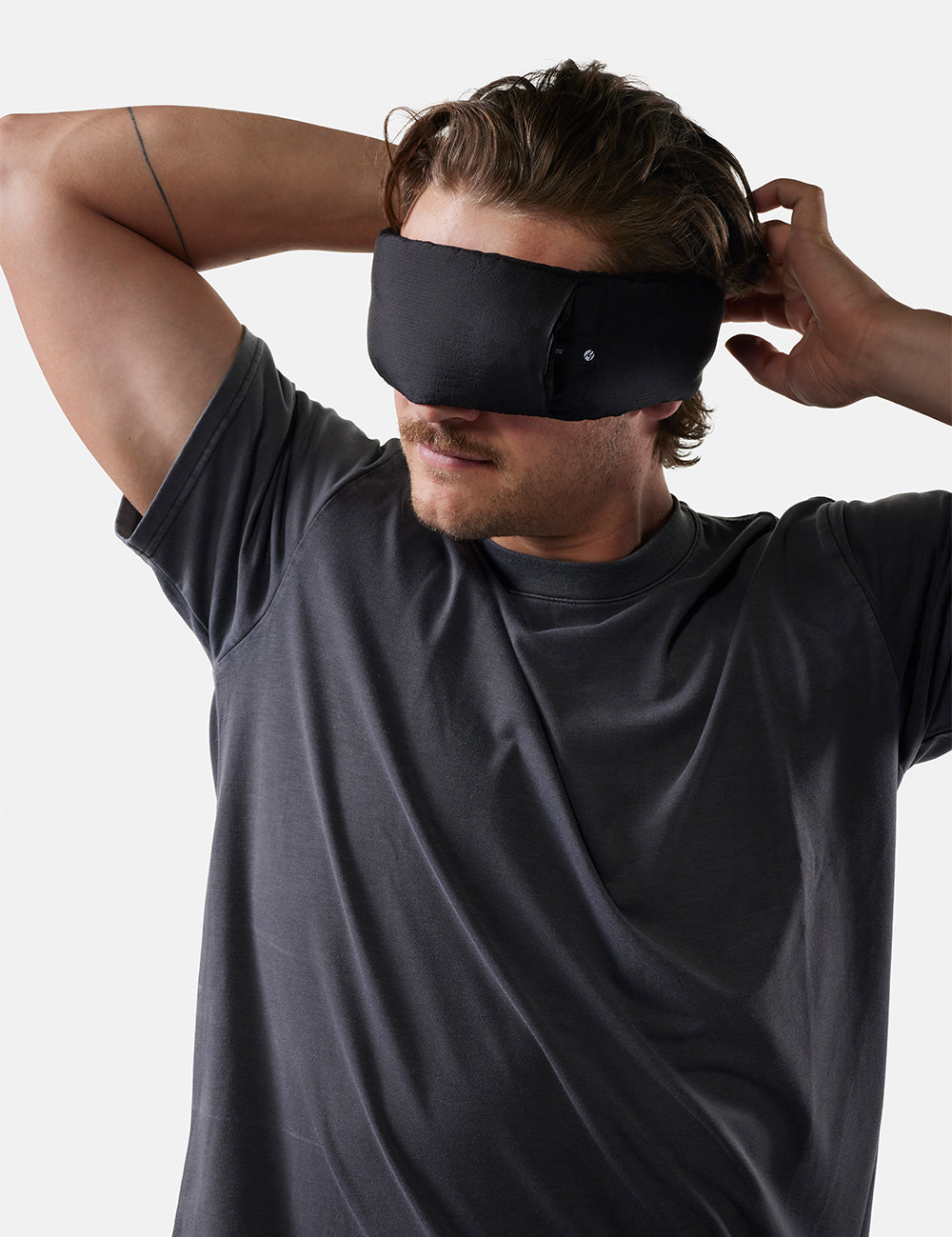 Man wearing a black sleep mask against a plain background