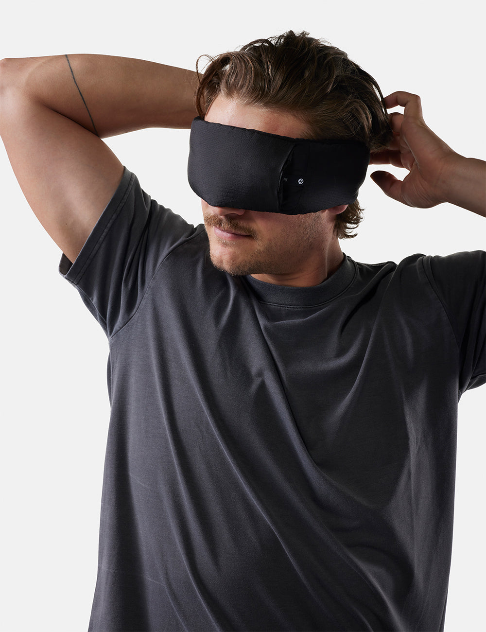 Man wearing a black sleep mask against a plain background