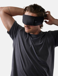 Man wearing a black sleep mask against a plain background