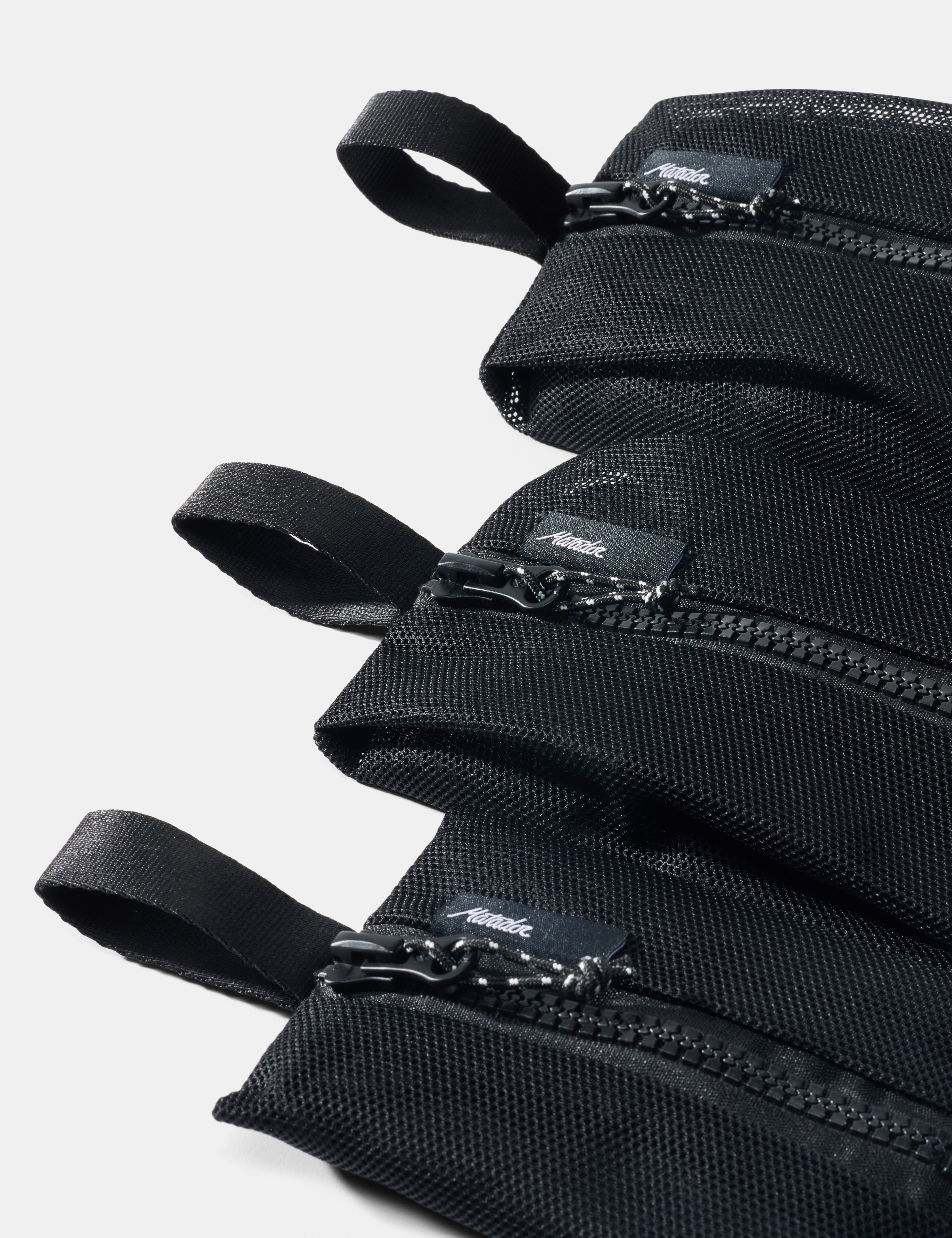 Stack of black pouches with zippers on a light gray background