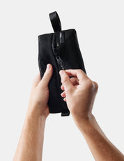 Black pouch with a zipper held by hands against a light background