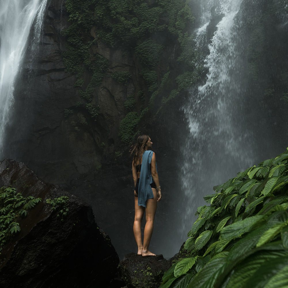 Woman standing in front of tropical waterfall with slate towel over her shoulder