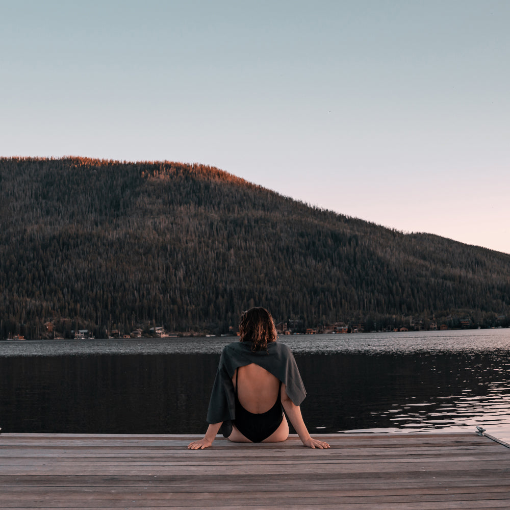 Woman sitting on the end of an evening lake dock, wearing charcoal towel over her shoulders
