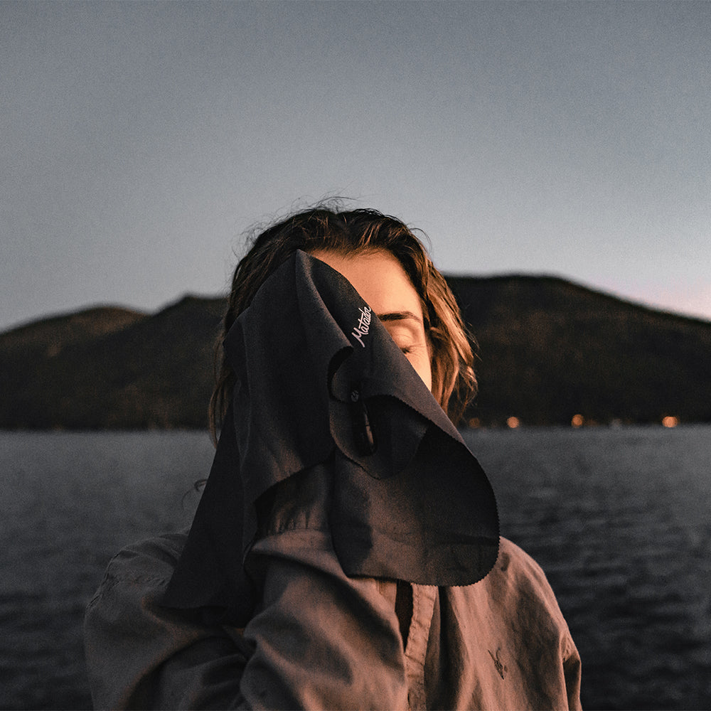 woman in front of evening alpine lake, wiping face with small towel