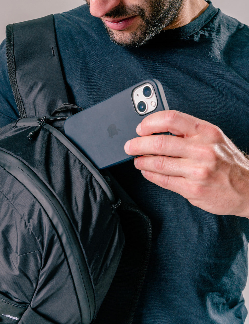 man placing phone into zipper pocket of black backpack