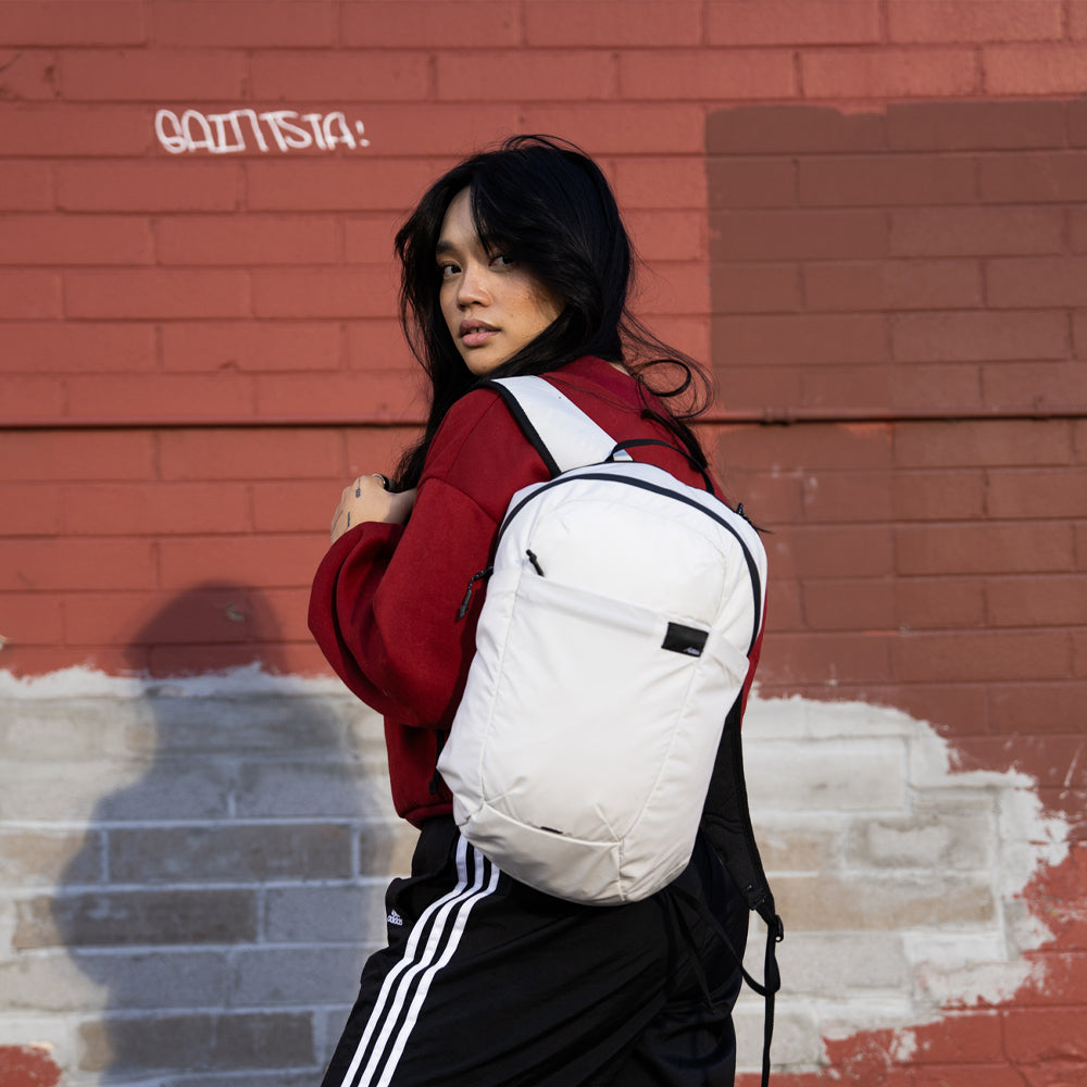 Woman in red, wearing white backpack in front of brick wall