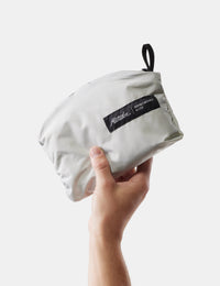 Hand holding a white pouch with a brand label on a white background
