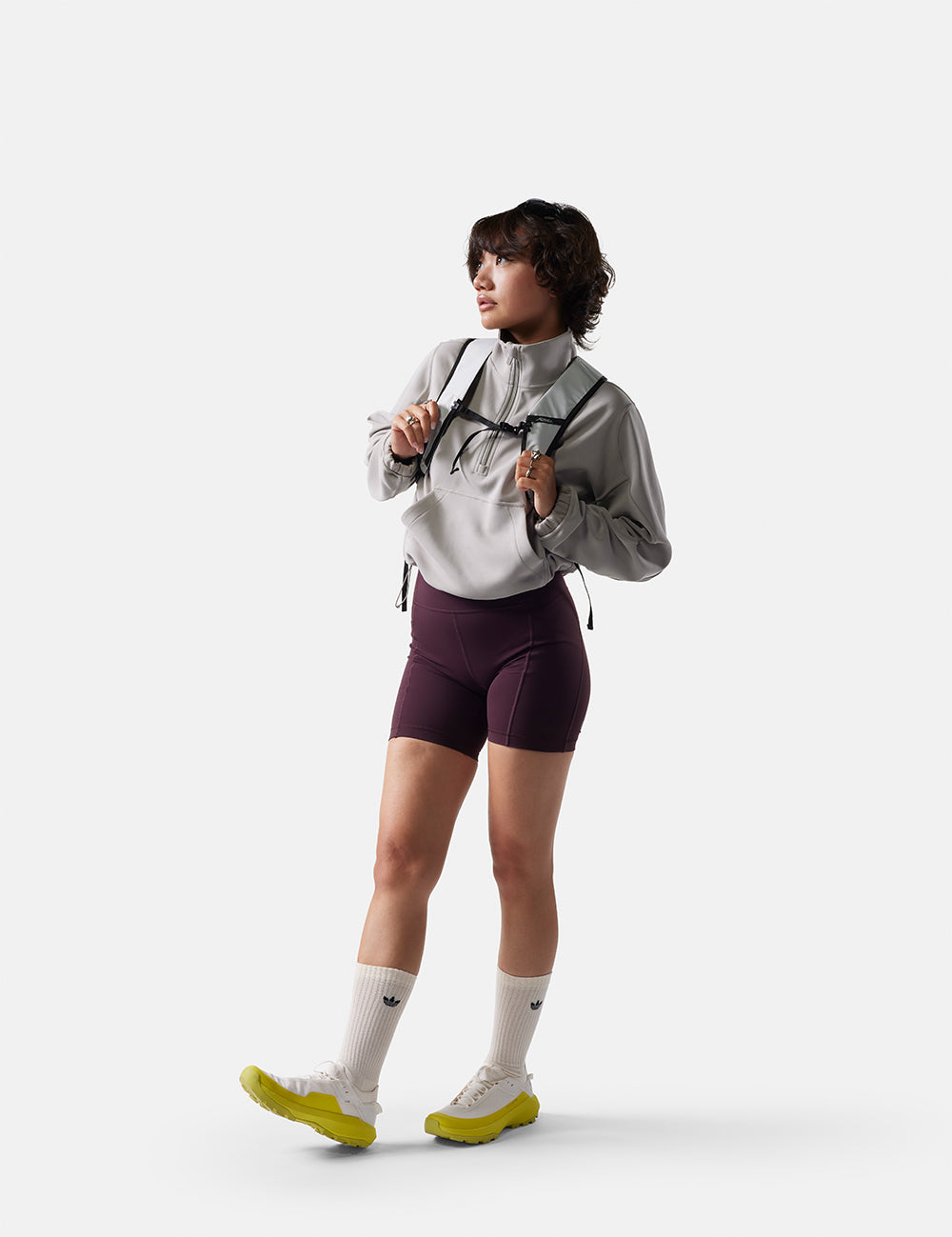 Person wearing a gray jacket, purple shorts, and green shoes on a white background