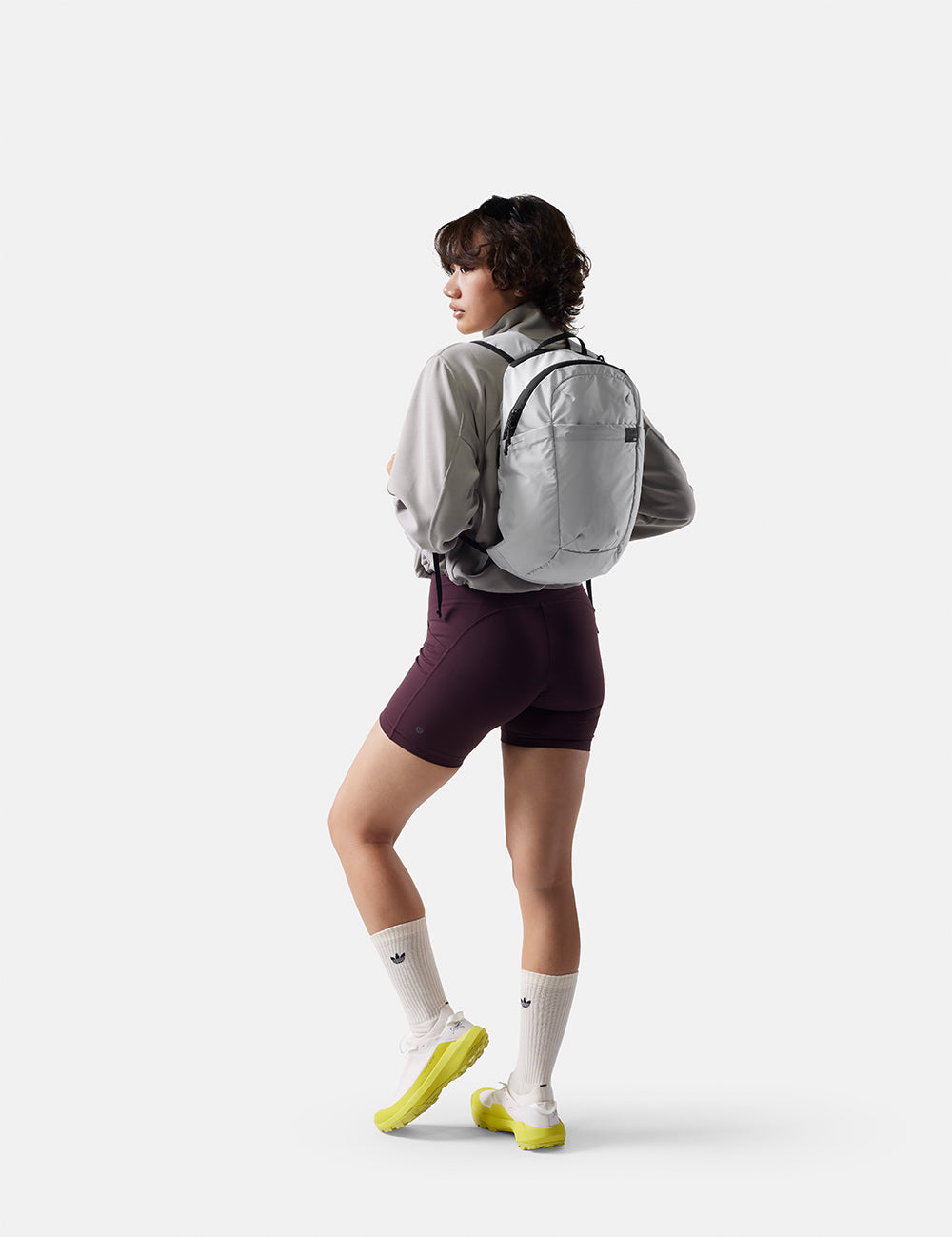 Person wearing a gray backpack and purple shorts on a white background