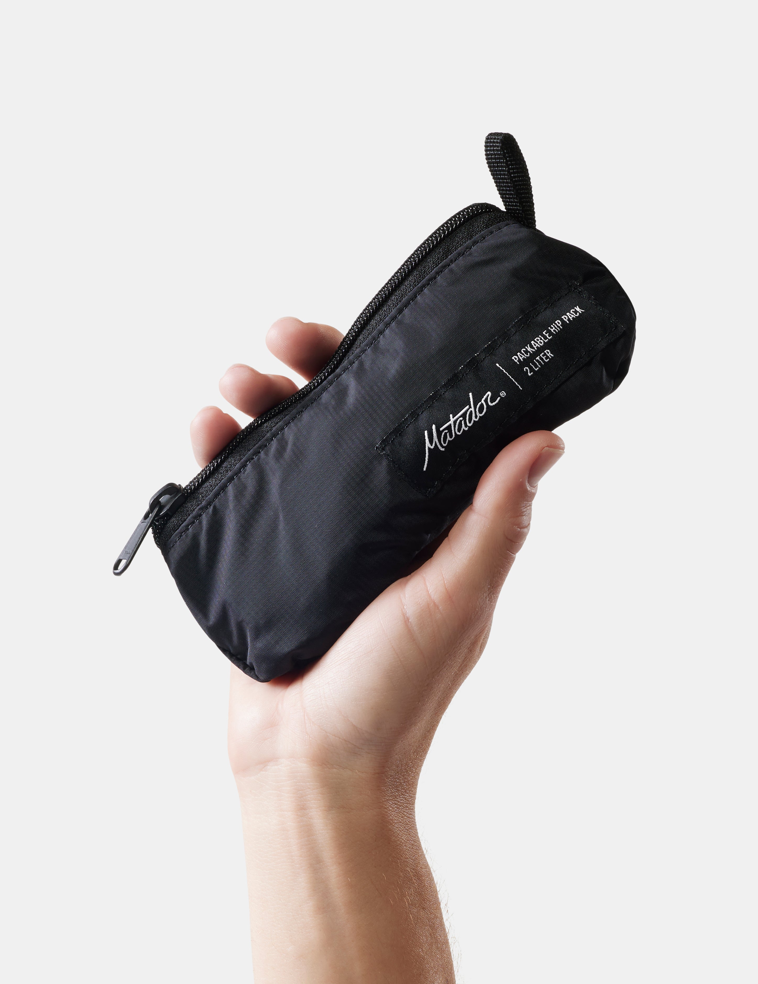 Hand holding a black pouch with 'Matador' branding on a light background
