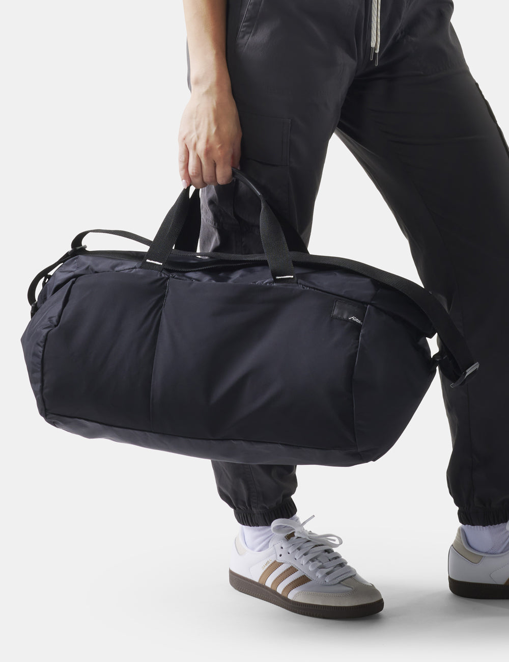 black duffle being held down at a woman&#39;s side on white background