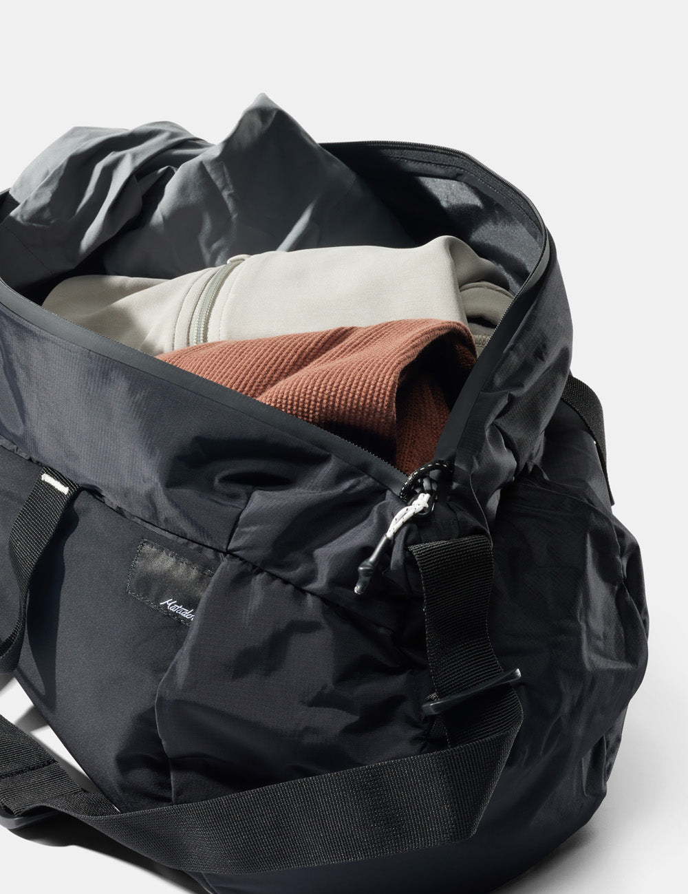 unzipped black duffle with clothing visible on white background