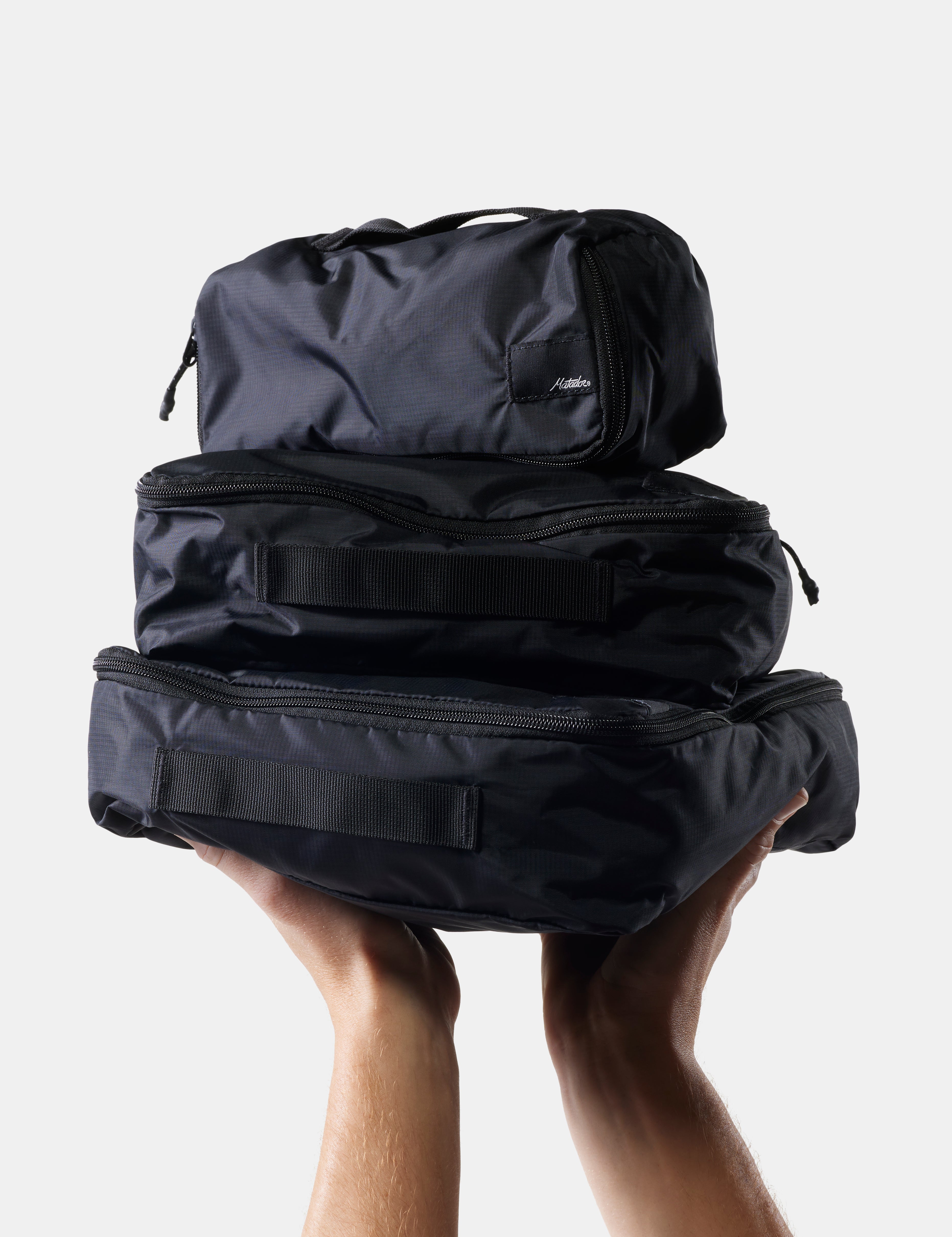 Stack of black packing cubes held by a person against a light background