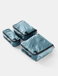 Set of three blue packing cubes with black zippers on a light gray background