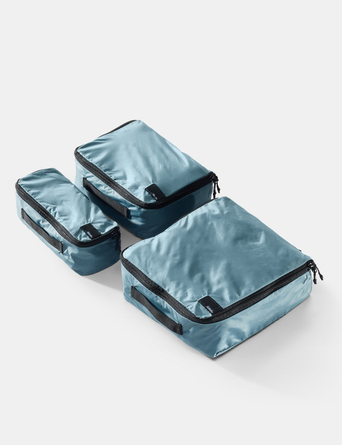 Set of three blue packing cubes with black zippers on a light gray background