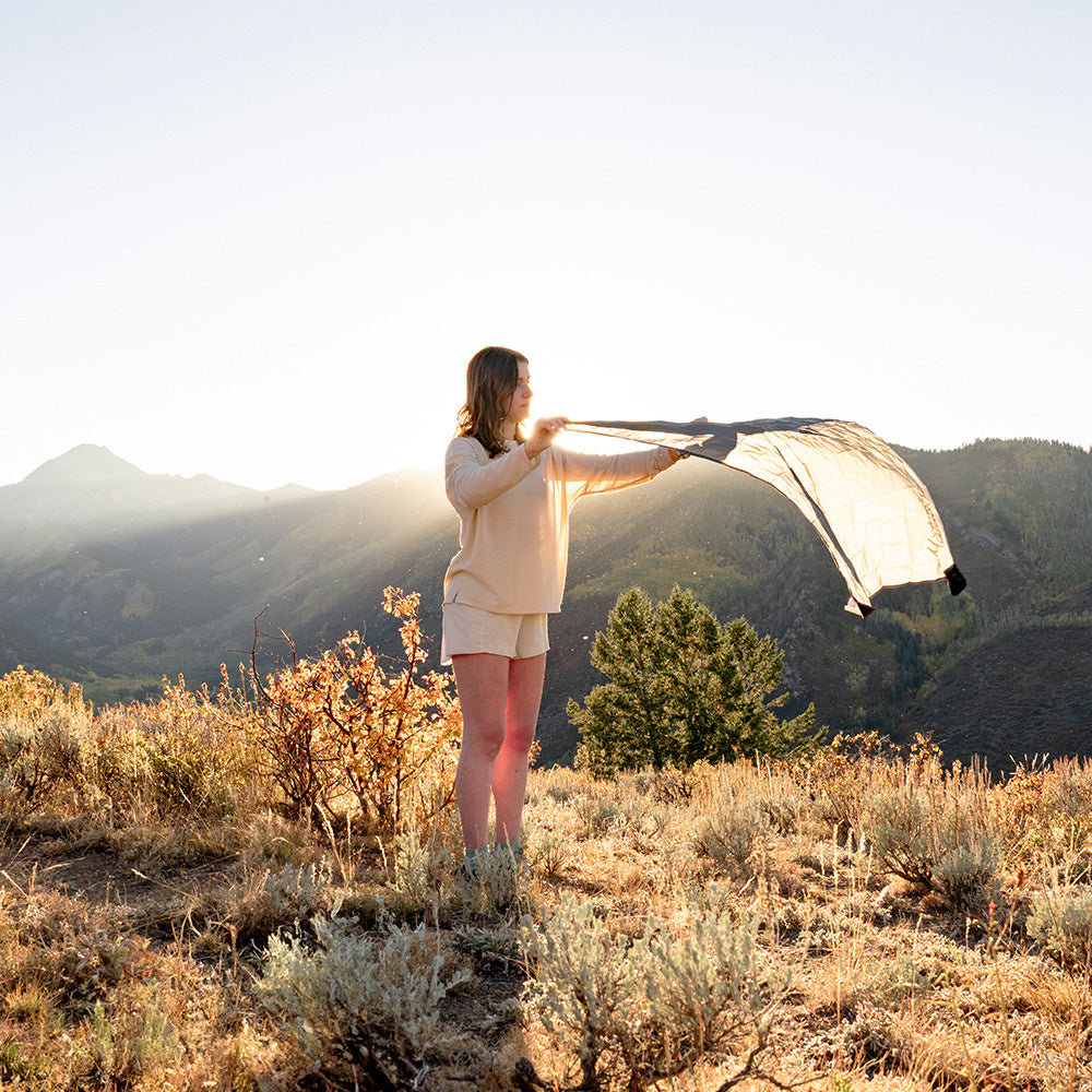 woman opening pocket blanket mini on sunset mountainside 
