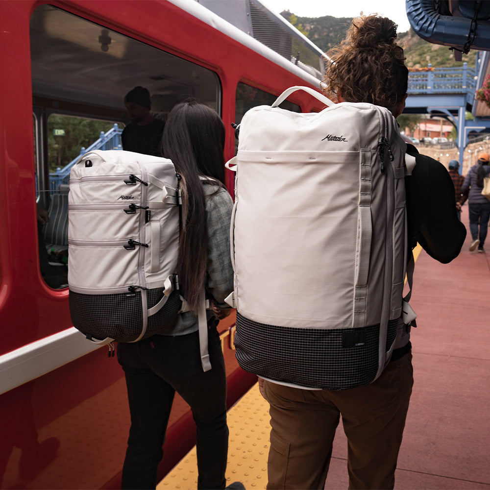 two people on train platform wearing white backpacks