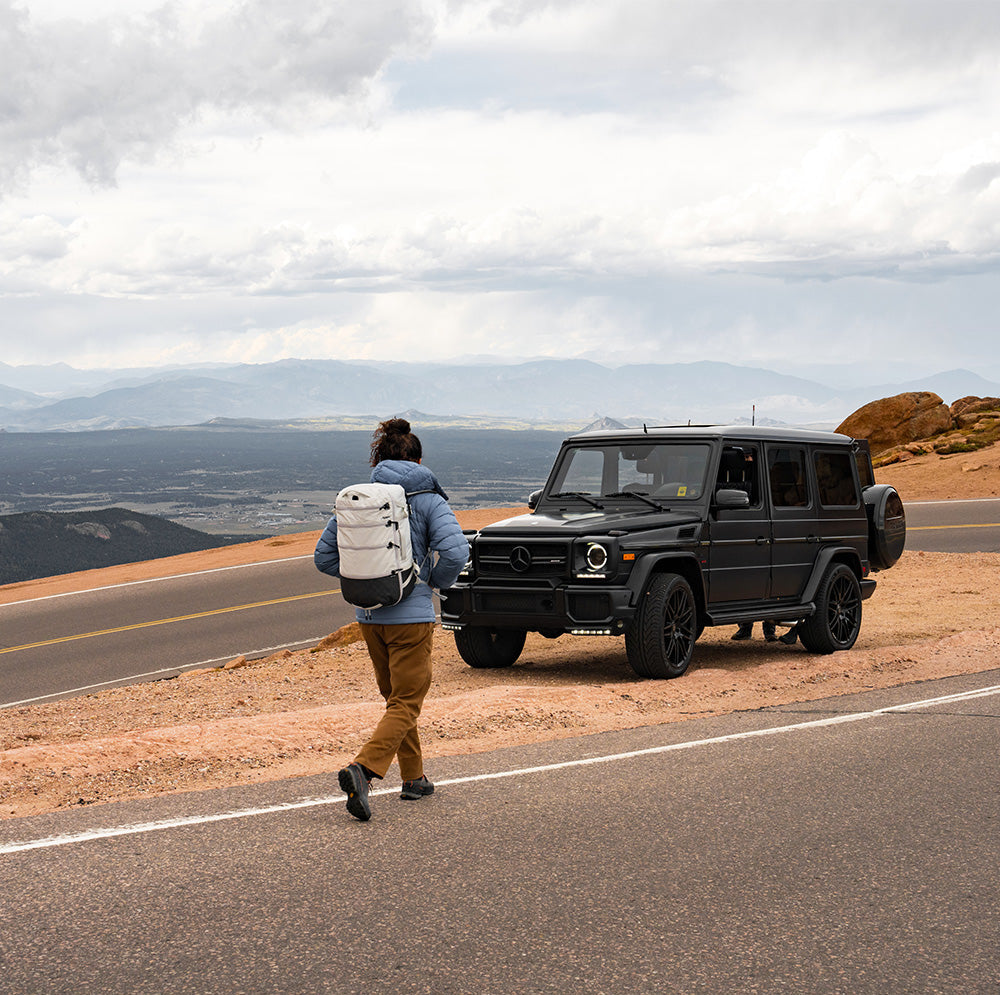man walking to vehicle on mountain road wearing white backpack