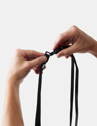 Close-up of hands tying a black lanyard against a white background