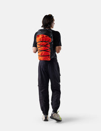 Person wearing a black outfit with an orange and red backpack on a white background