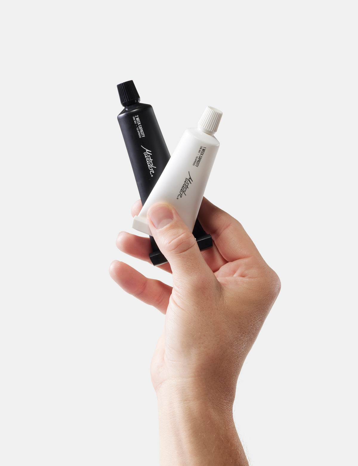 Hand holding two toothpaste tubes against a white background