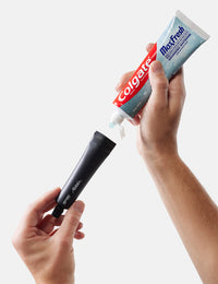 Colgate MaxFresh toothpaste tube being squeezed onto a black applicator against a white background