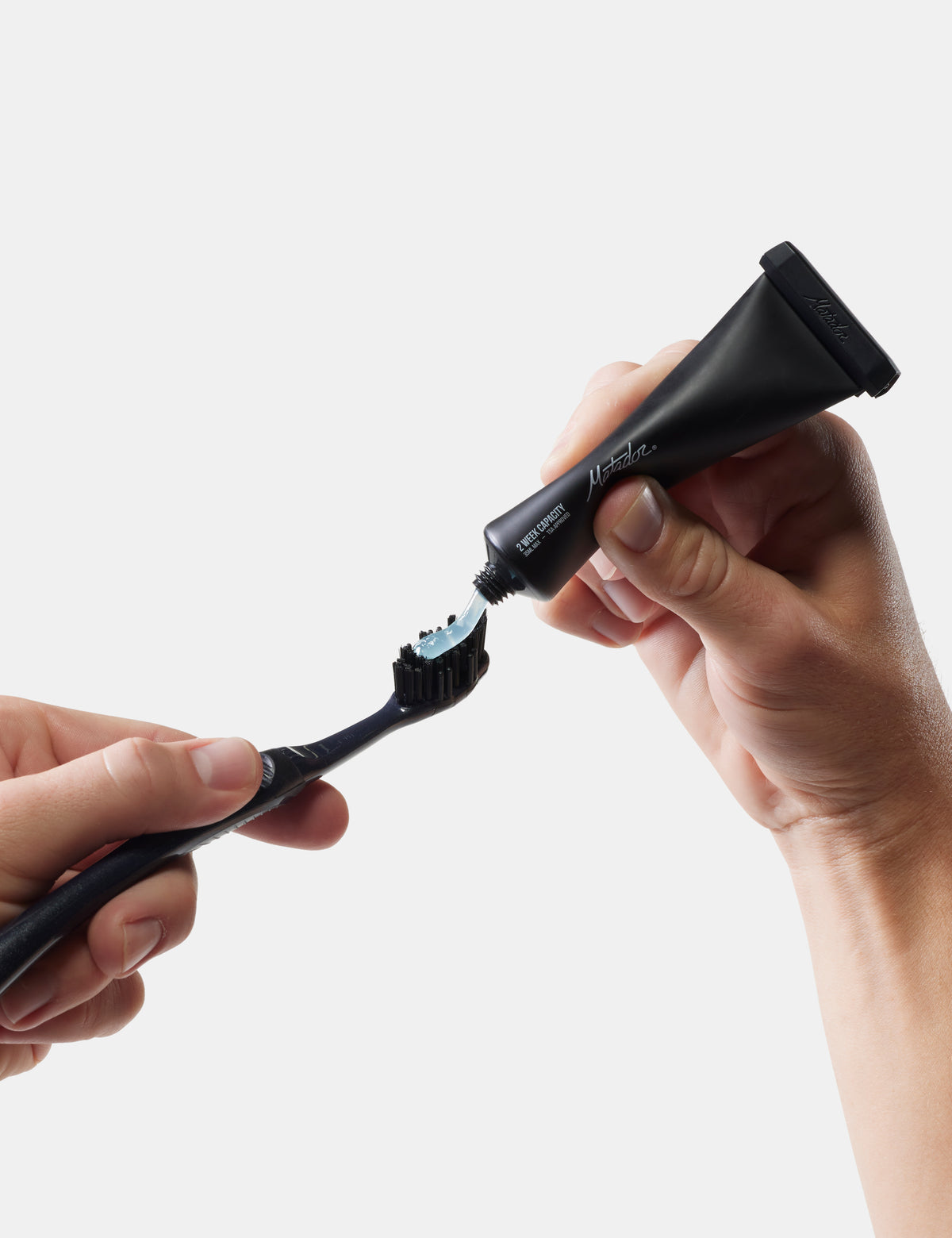 Person applying toothpaste to a black toothbrush on a white background
