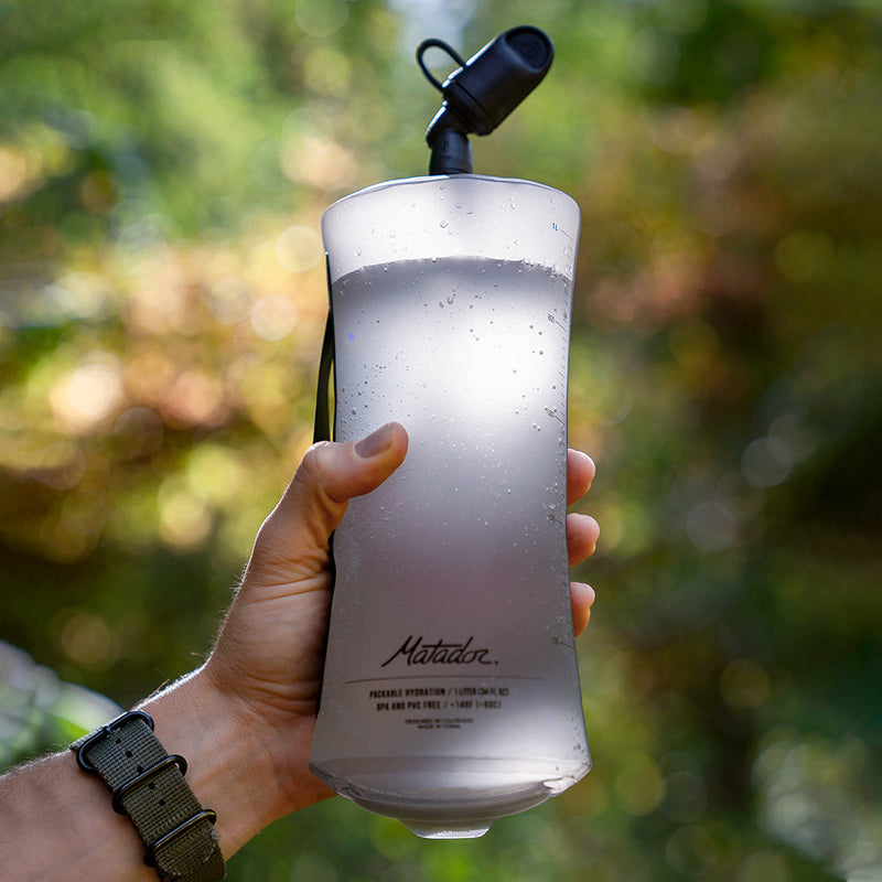 hand holding full water bottle in front of nature background