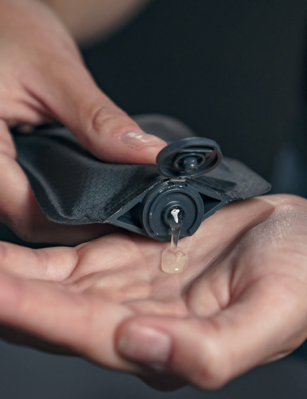 hands squeezing clear liquid from black toiletry bottle