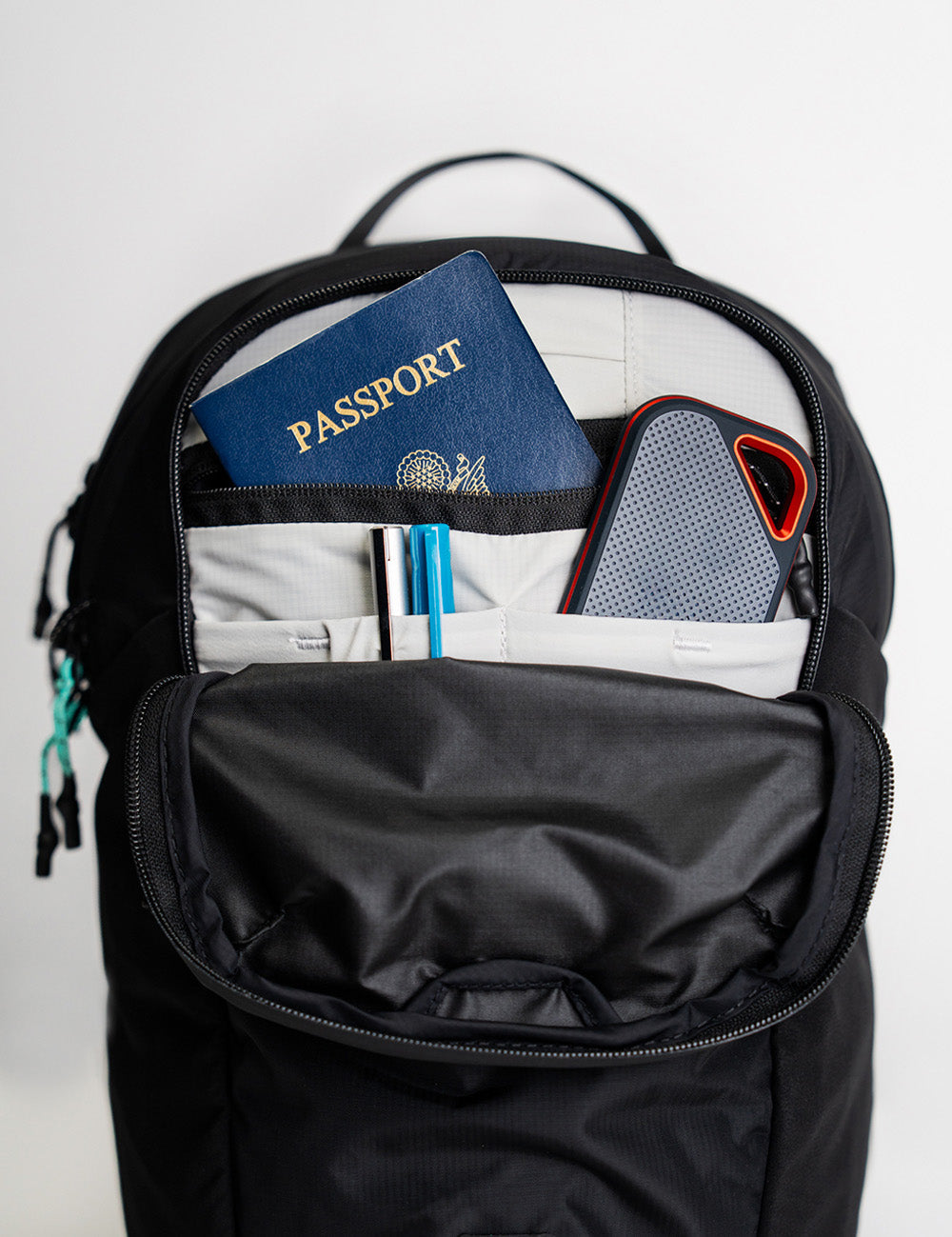 detail view of inside pockets of black backpack full of pens, external hard drive and passport
